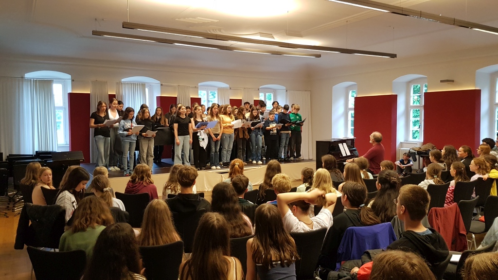 Schülerchor singt auf Bühne in Aula während Schülerversammlung