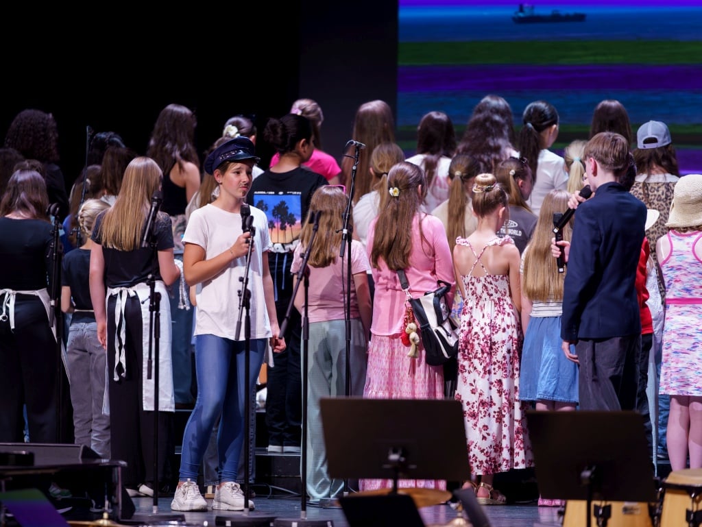 Aufführung des Kinderchors Kinderchor auf Bühne, bunt gekleidet, vor großem Publikum